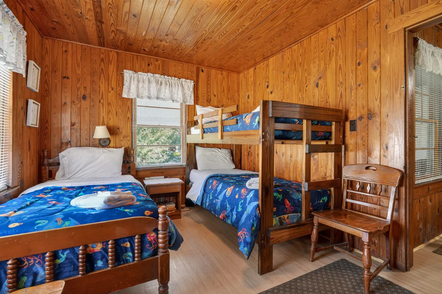 Bedroom with knotty pine wood-paneled walls and ceiling, featuring a twin bed and a set of wooden bunk beds.