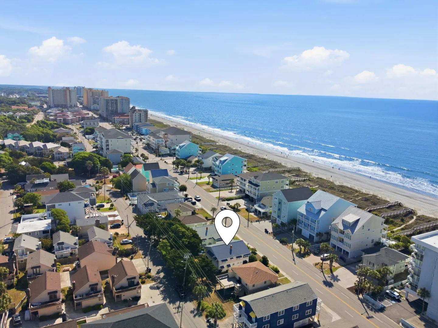 Aerial view of a coastal neighborhood with a location pin over a home just across the street from the sandy beach and ocean.
