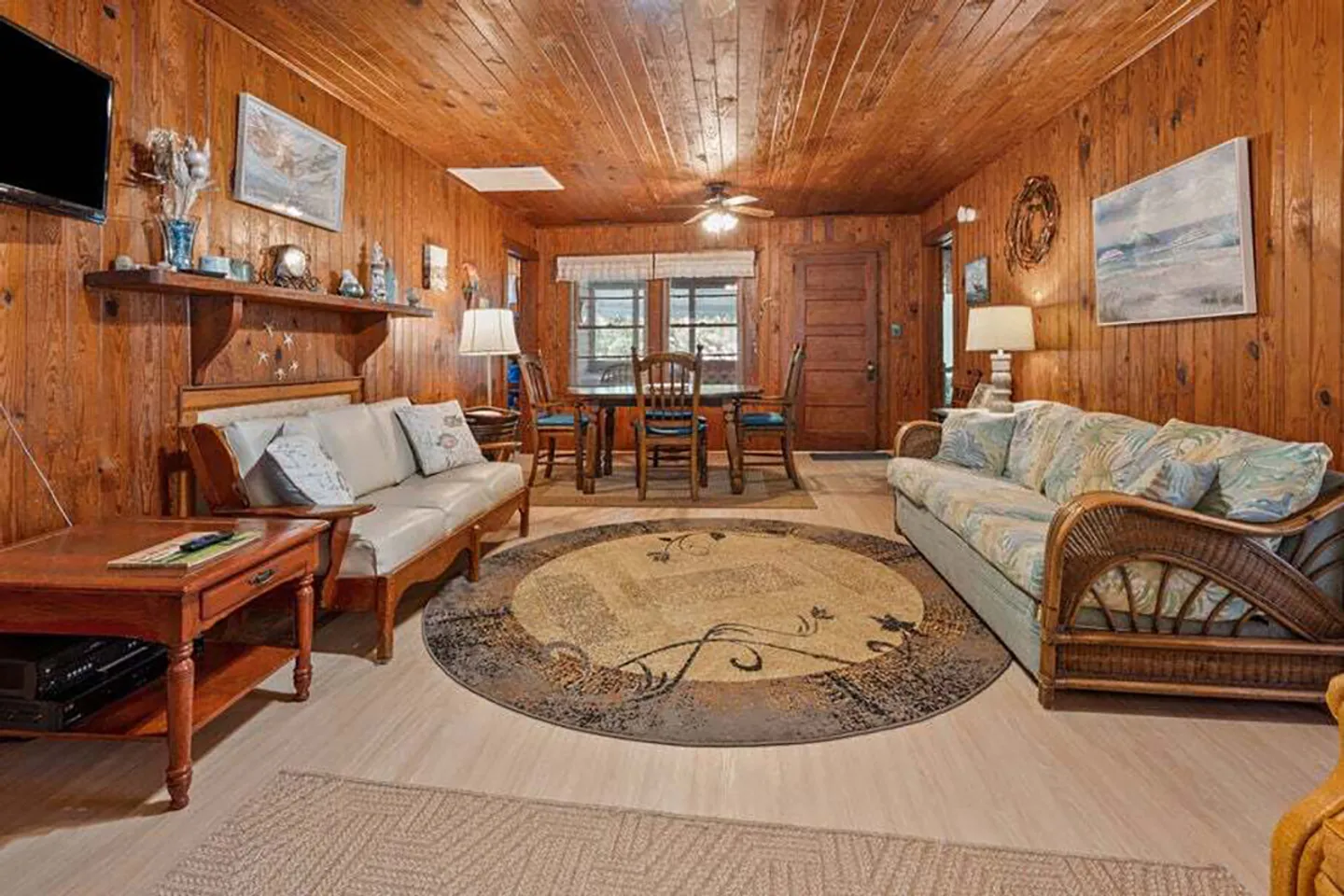 Living and dining area featuring wood-paneled walls and ceiling, two sofas, a round rug, and a dining table in the background.