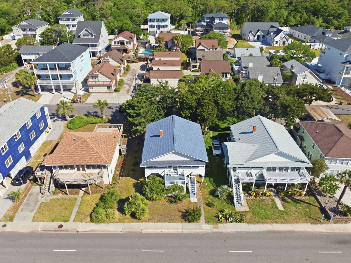 Aerial view of a coastal neighborhood showing rows of beach-style houses along a paved street under bright daylight.