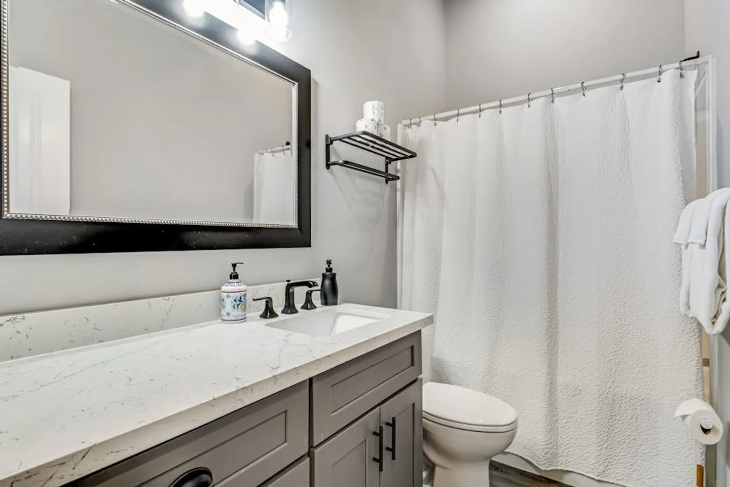 Bathroom vanity with a dark frame mirror, toilet, and shower with a white curtain.