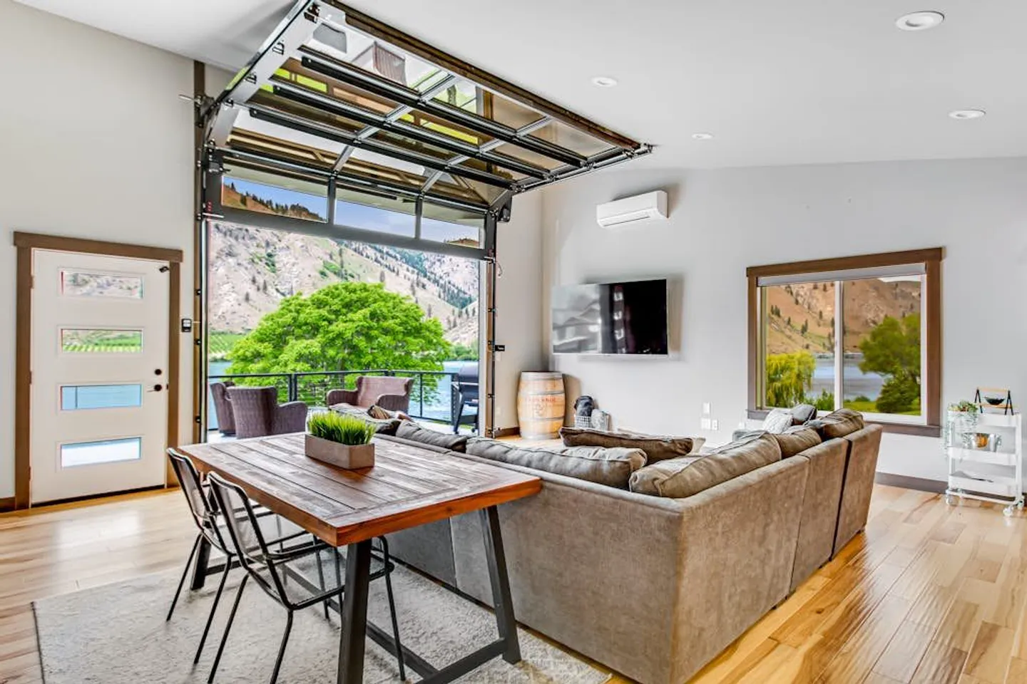 Living room with an open glass roll-up garage door leading to a patio overlooking mountains and water.