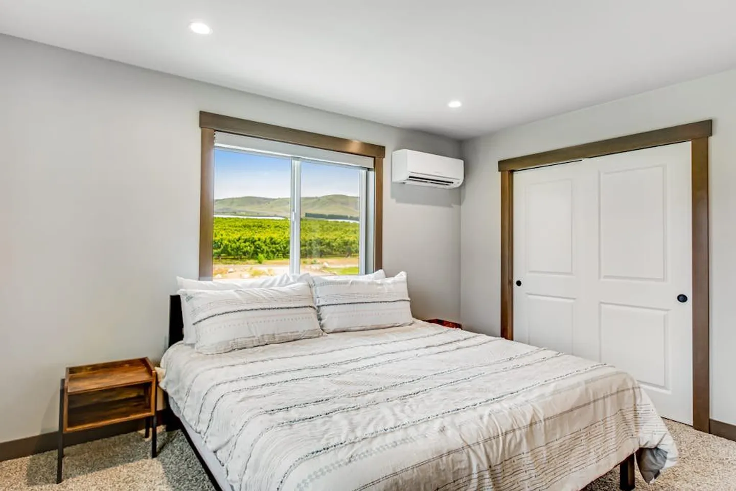 Bedroom with a made bed, carpet flooring, a closet with double doors, and a window overlooking an orchard and hills.