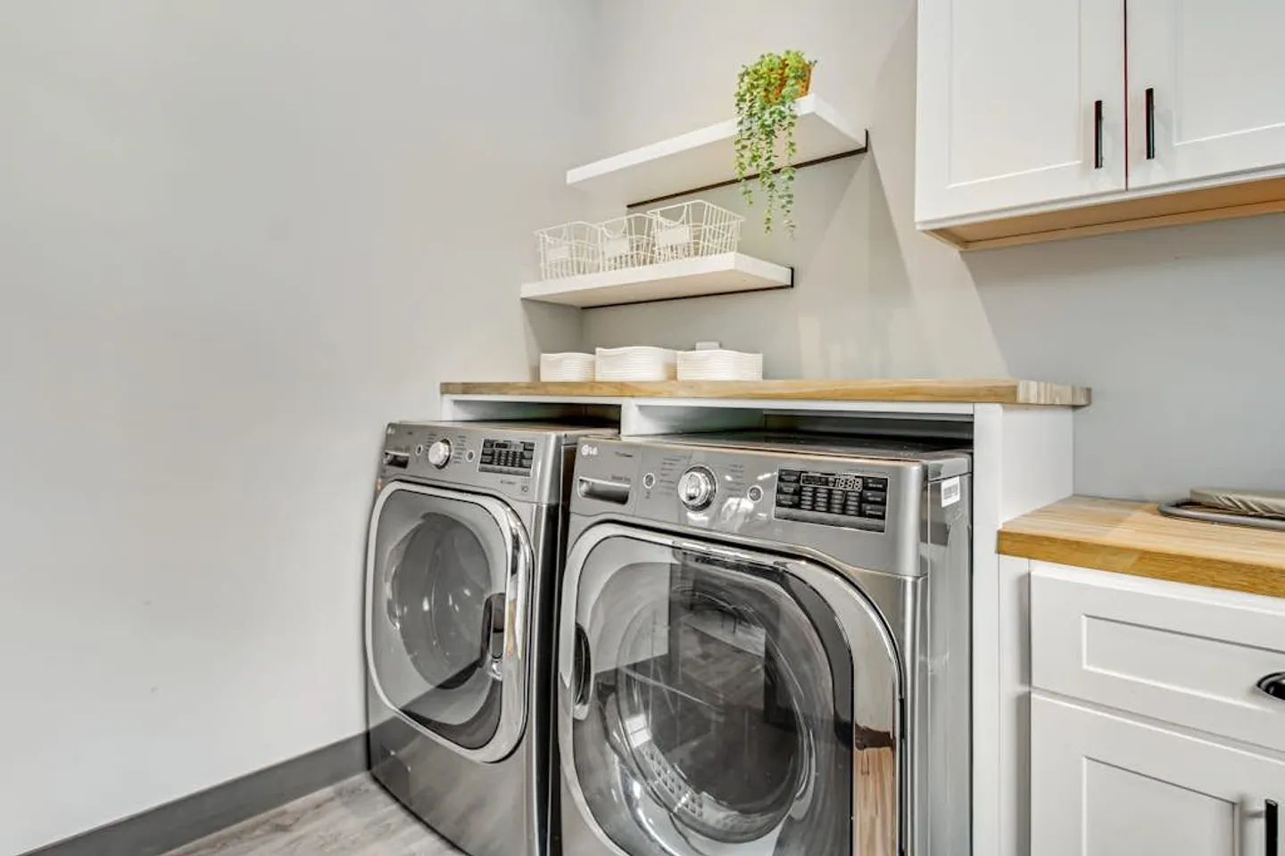 Front-loading stainless steel washer and dryer installed under a wood-topped counter with floating shelves above.