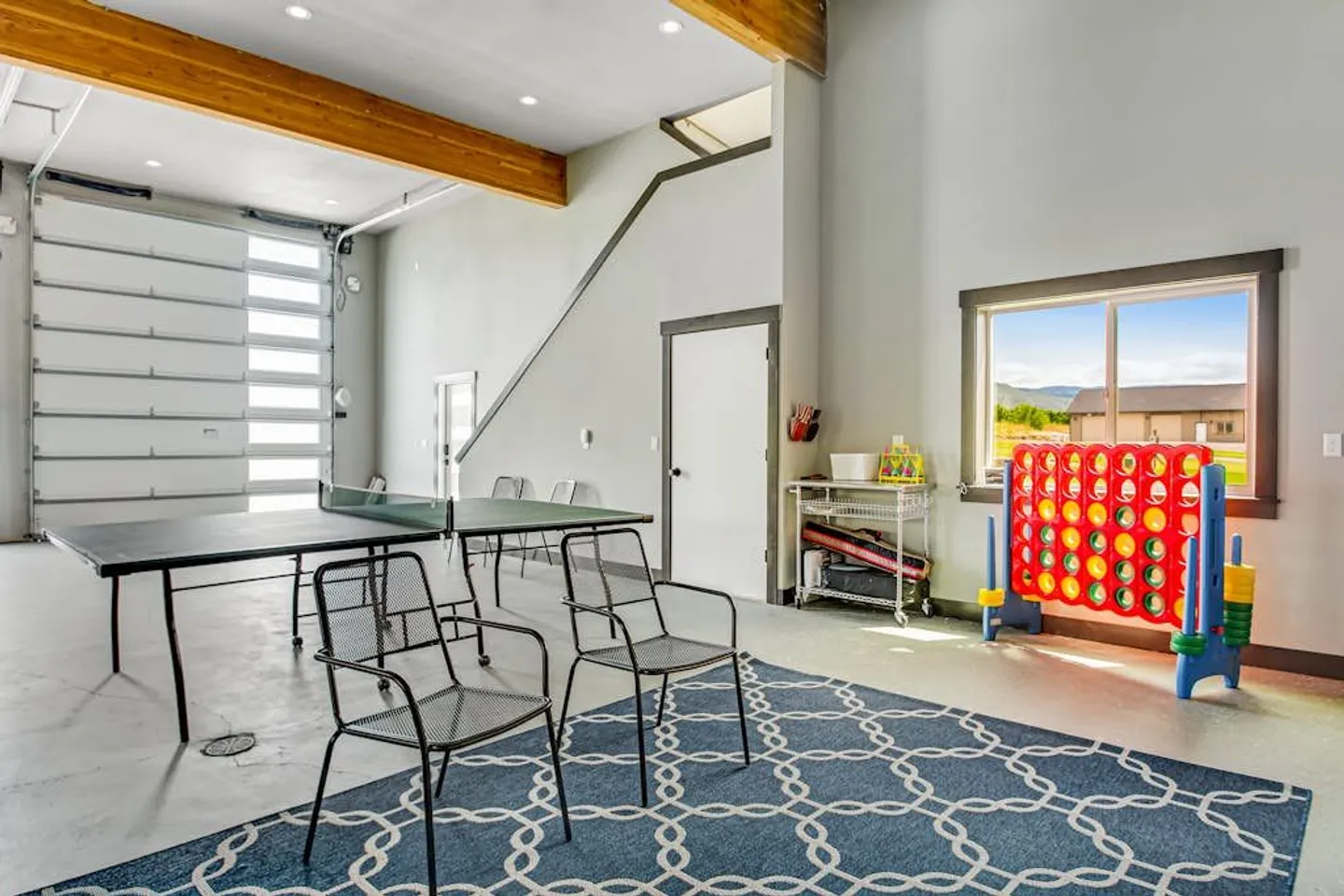 Game room featuring a ping pong table, metal chairs on a patterned blue rug, and a giant Connect Four set by a window.