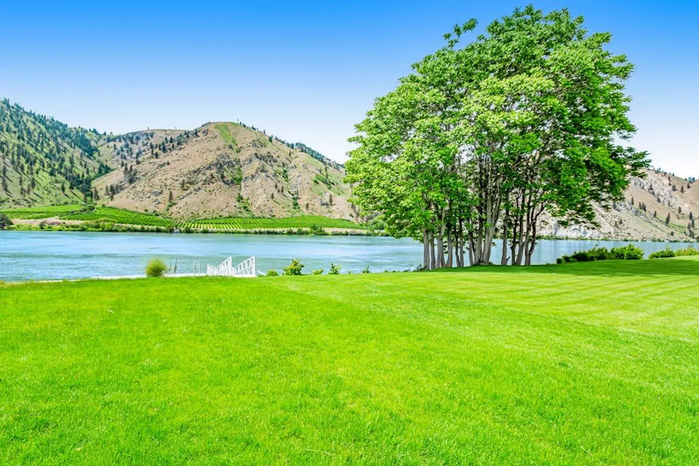 A wide view across an expansive green lawn leading to a body of water with hills in the background.