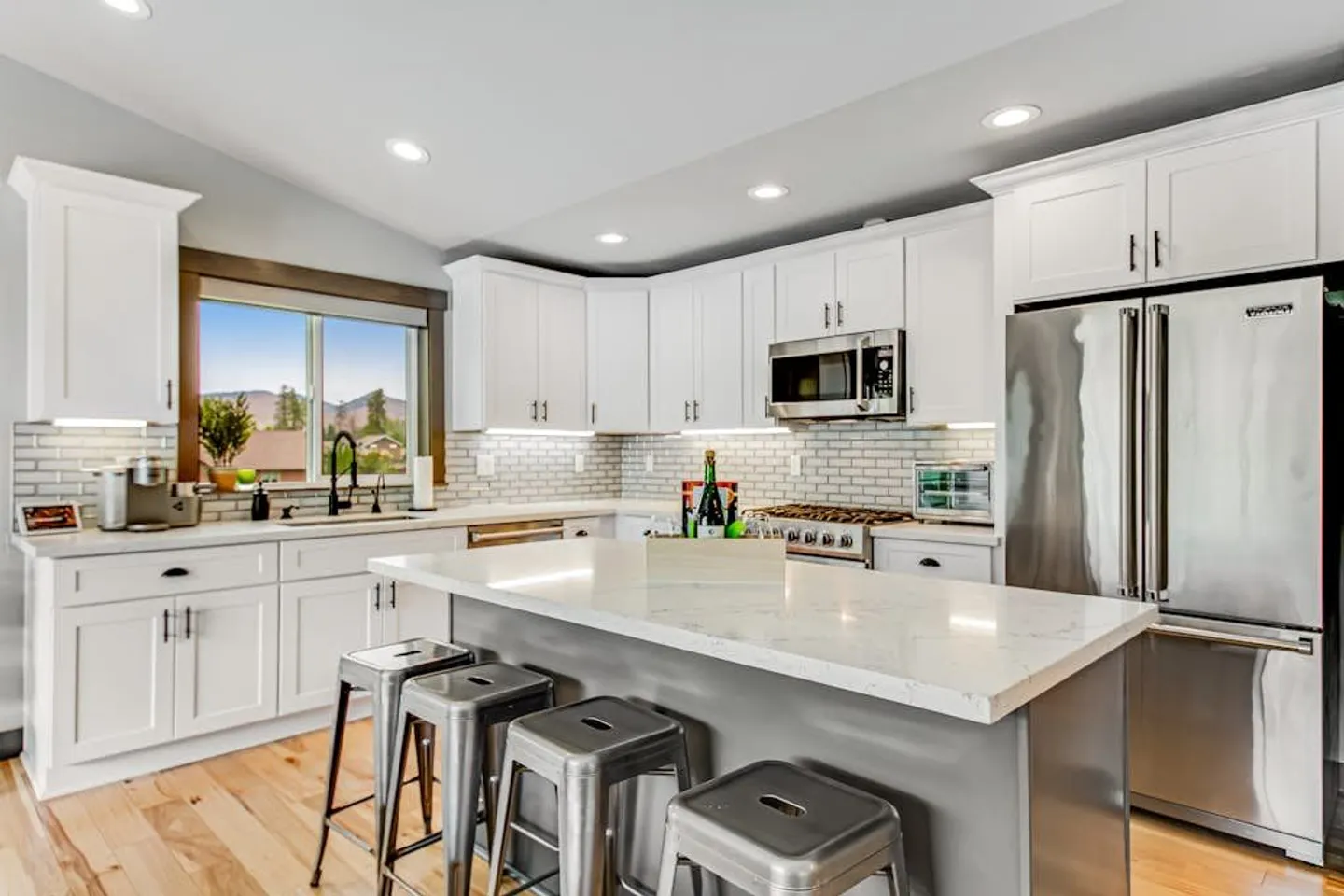 Bright kitchen featuring white shaker cabinets, subway tile backsplash, stainless steel appliances, and a central island with metal barstools.