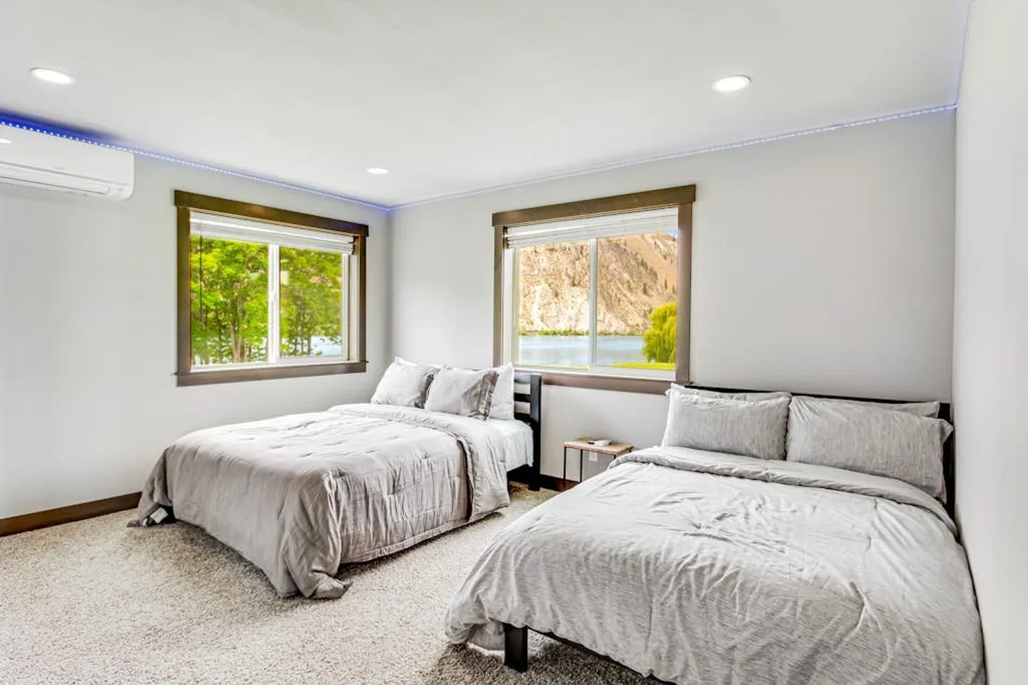 Bedroom with two beds, carpeted floor, and windows offering views of a lake and hills.