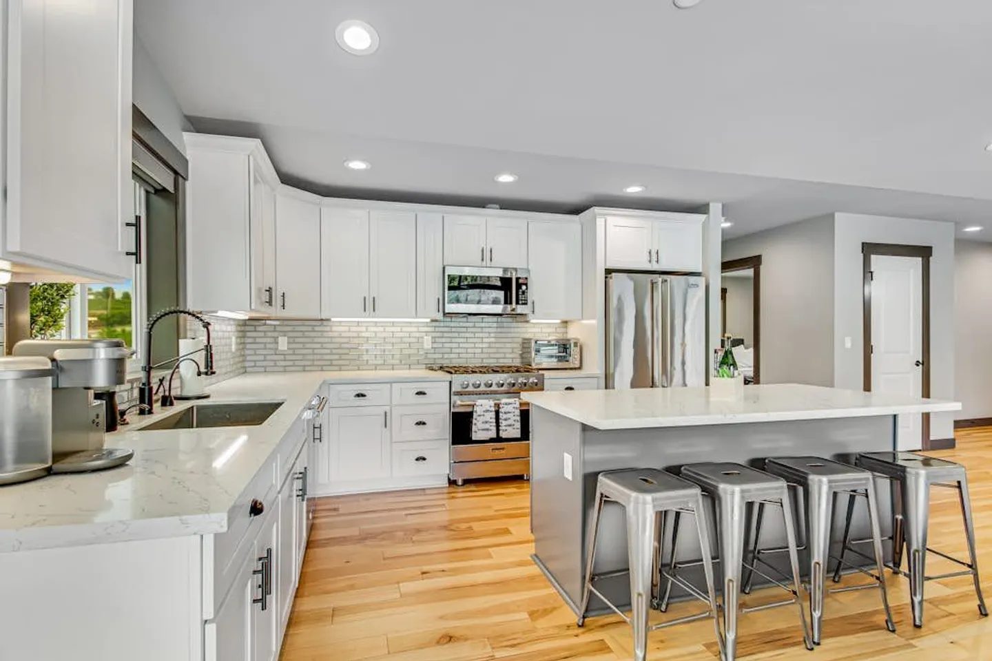 Bright kitchen featuring white shaker cabinets, light countertops, an island with metal barstools, and stainless steel appliances.