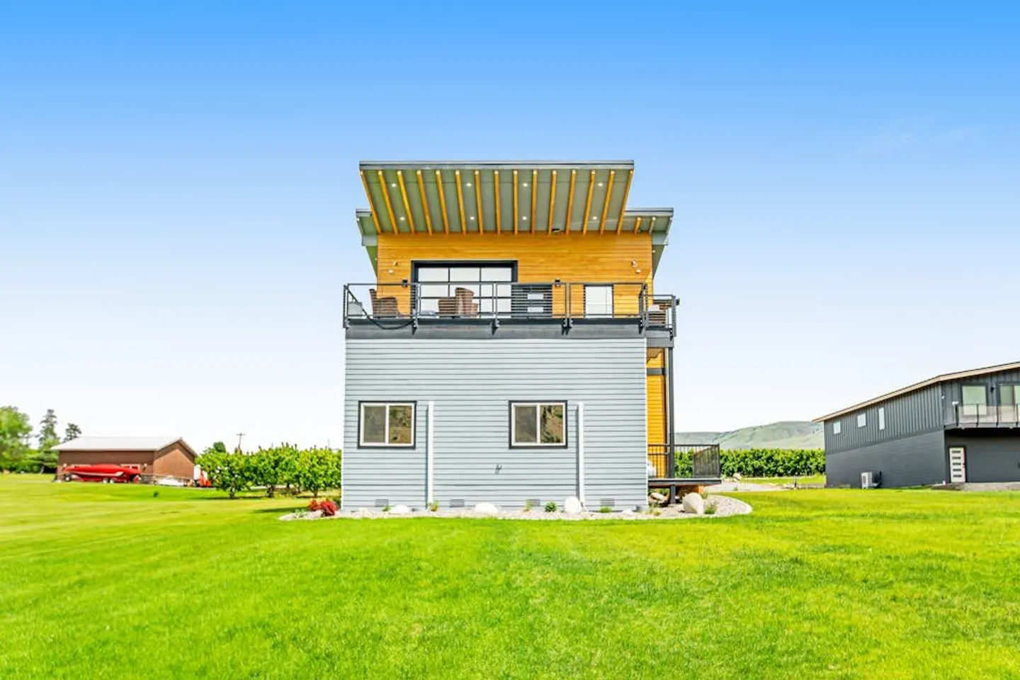 Exterior rear view of a modern two-story home with a green lawn under a clear blue sky.