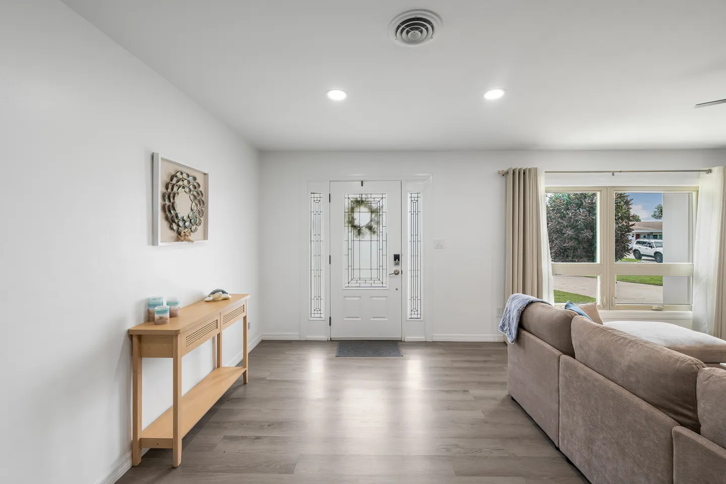 Front entryway with a white front door, decorative glass sidelights, wood-look flooring, and an adjoining living area.