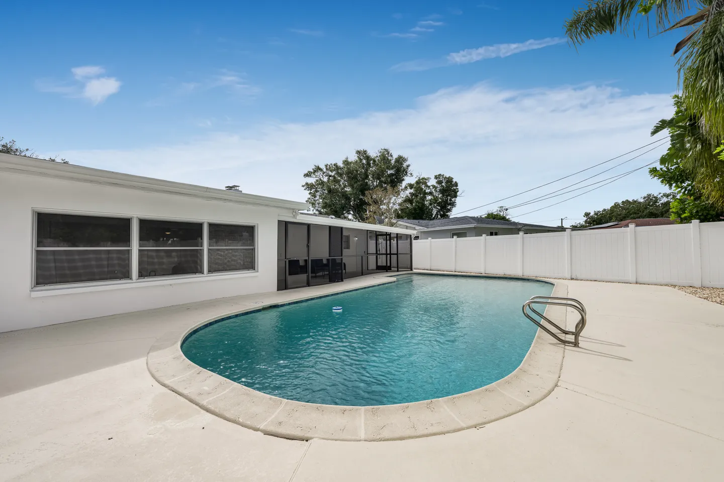 Outdoor swimming pool surrounded by a concrete patio and a white privacy fence adjacent to a white house.