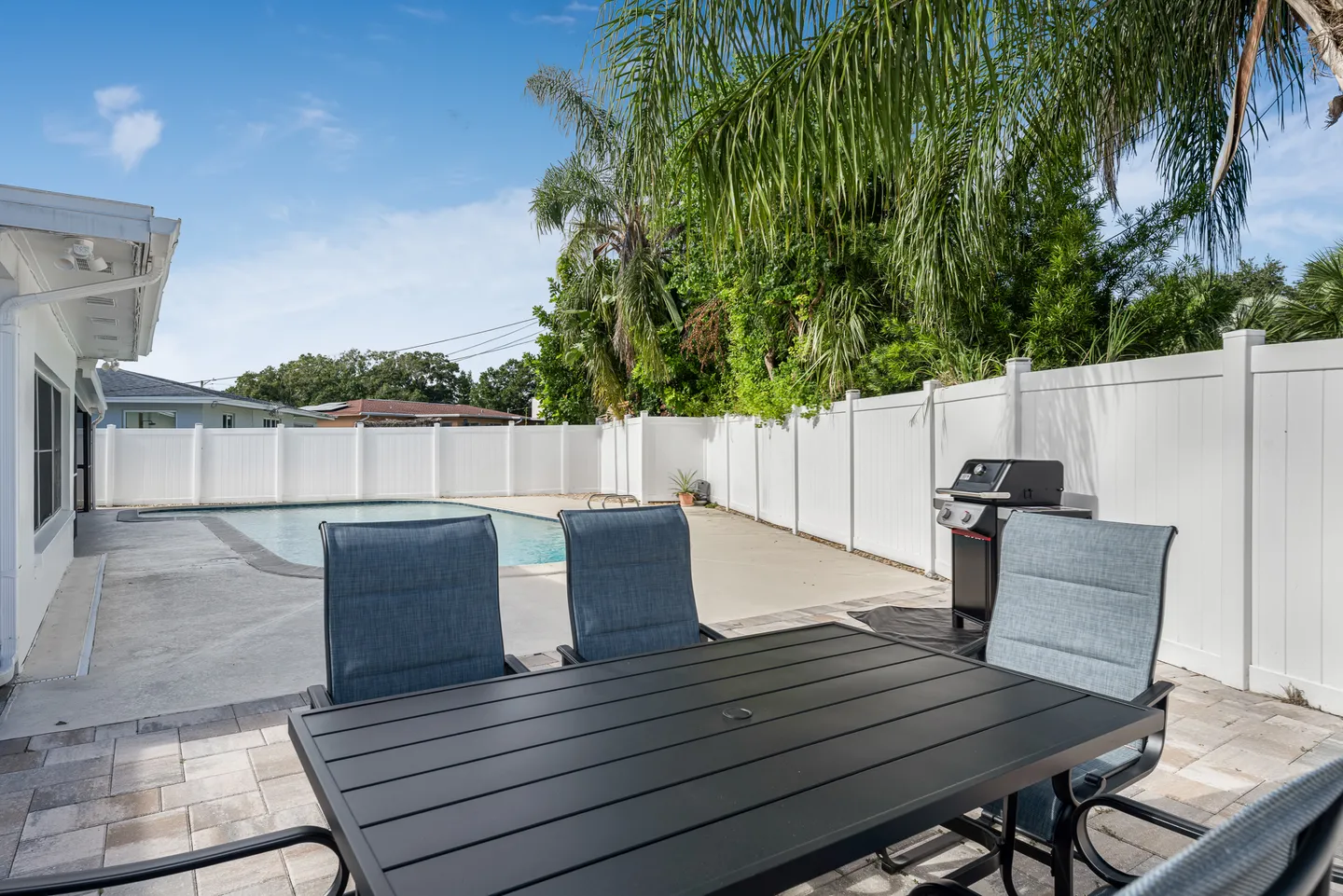 Fenced backyard patio featuring an outdoor dining table and chairs, a barbecue grill, and a swimming pool.