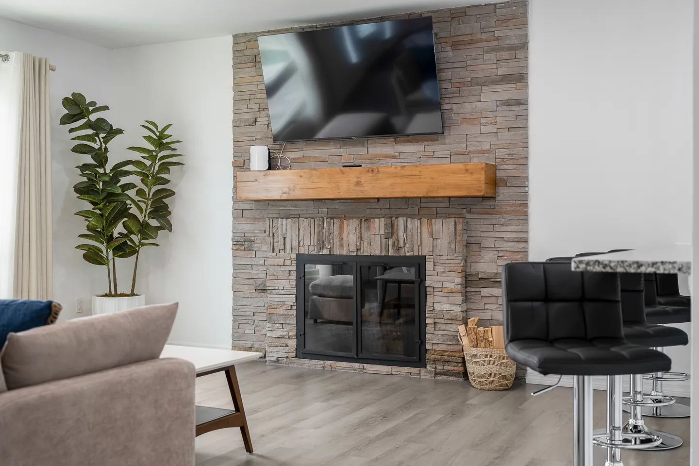Living room featuring a stacked stone fireplace with a thick wood mantel and wall-mounted TV above.