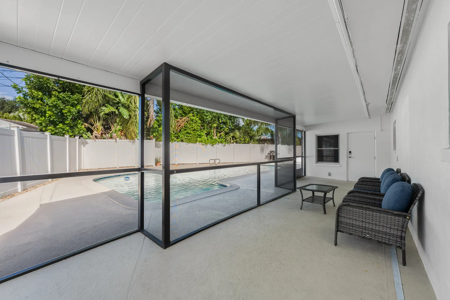 Covered patio with wicker seating overlooking a fenced backyard and swimming pool through a screen.