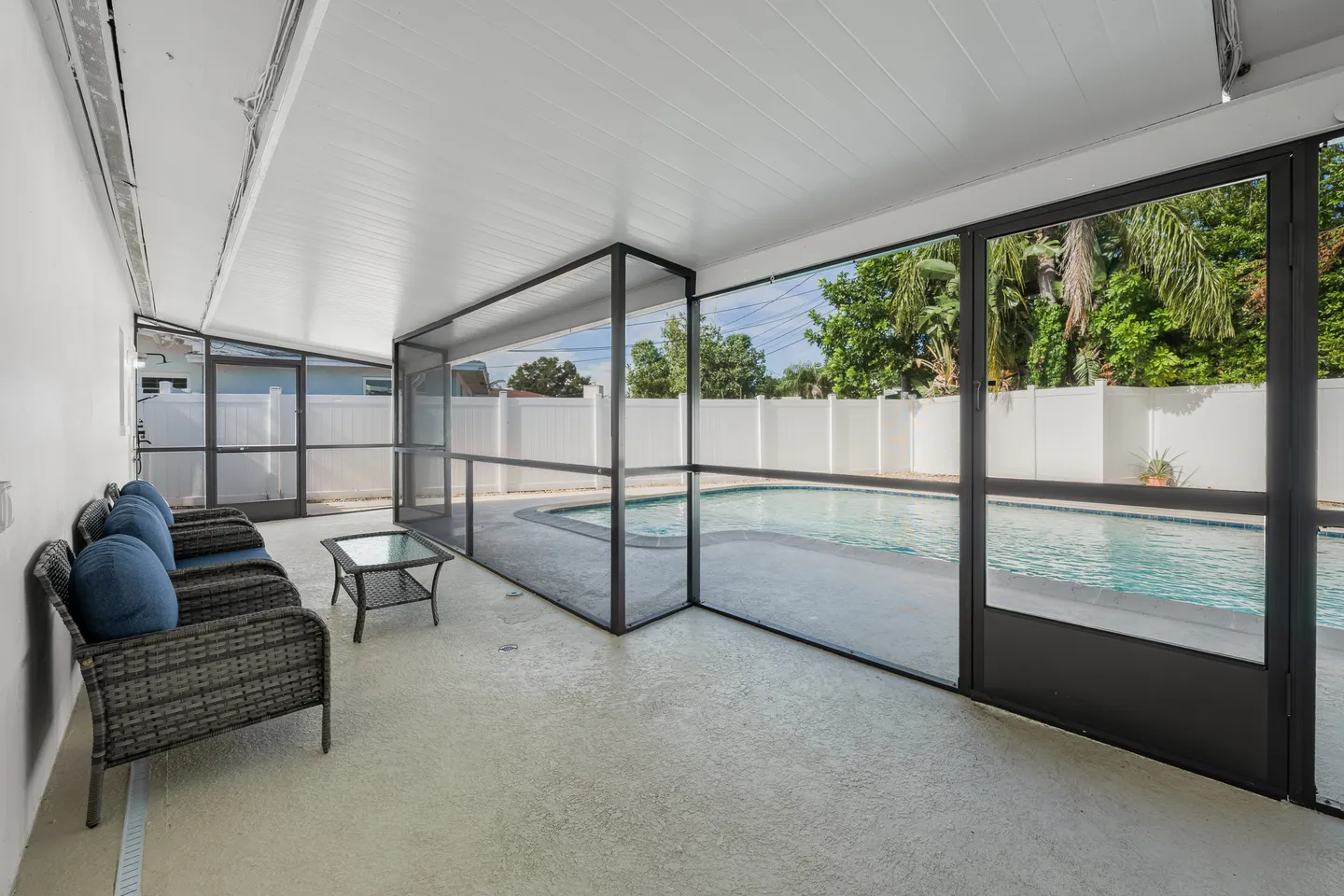 Screened-in patio with outdoor seating overlooking a swimming pool and fenced backyard.