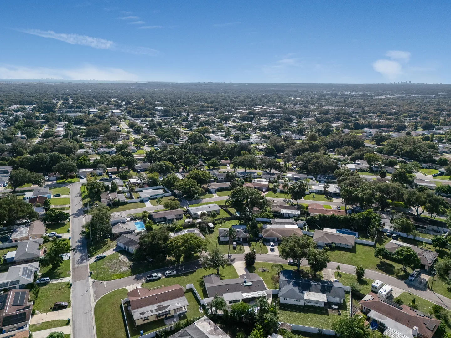 High aerial view of a residential neighborhood with single-family homes, mature trees, and streets stretching toward the horizon.