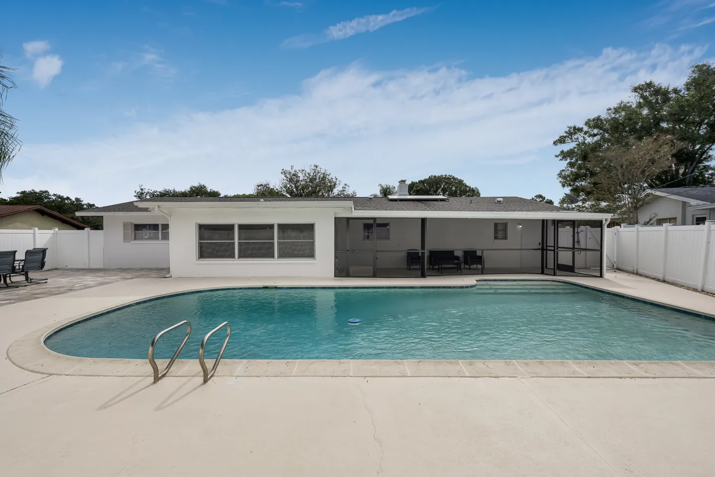 A large outdoor swimming pool in a fenced backyard behind a single-story house with a screened porch.