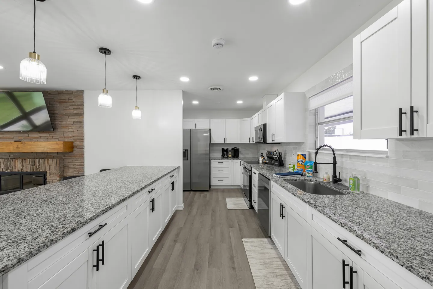 Modern kitchen with white shaker cabinets, speckled granite countertops, stainless steel appliances, and a large island.