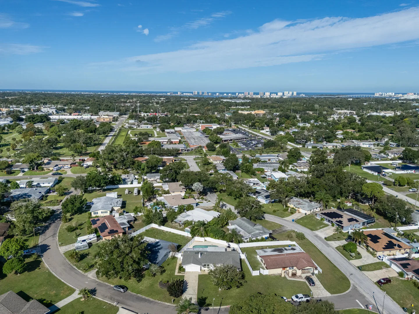 High aerial view of a residential neighborhood of single-story houses and mature trees stretching toward a distant coastal skyline.