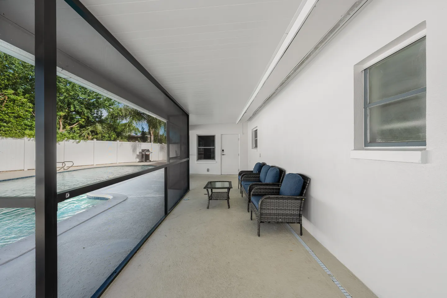 Screened-in covered patio with wicker armchairs, a coffee table, and views through mesh screening of an outdoor swimming pool.