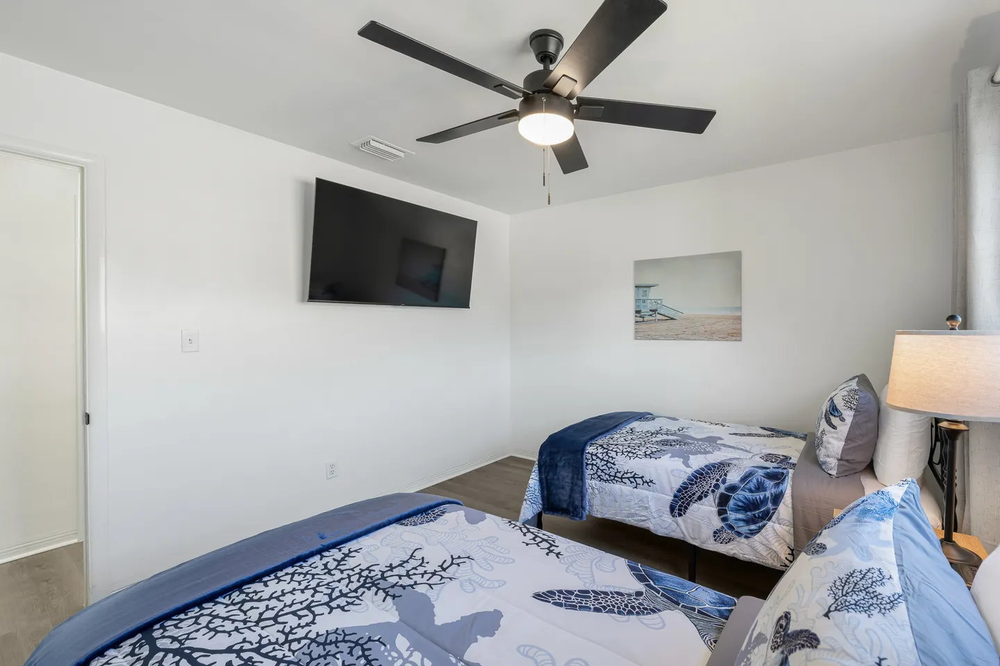 Bedroom with two twin beds dressed in sea turtle bedding, a wall-mounted TV, and a ceiling fan.