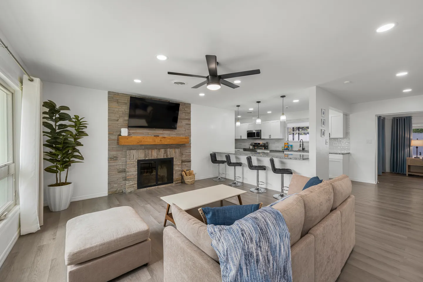 Open-concept living room with a stone fireplace, sofa, and view into the kitchen bar area.