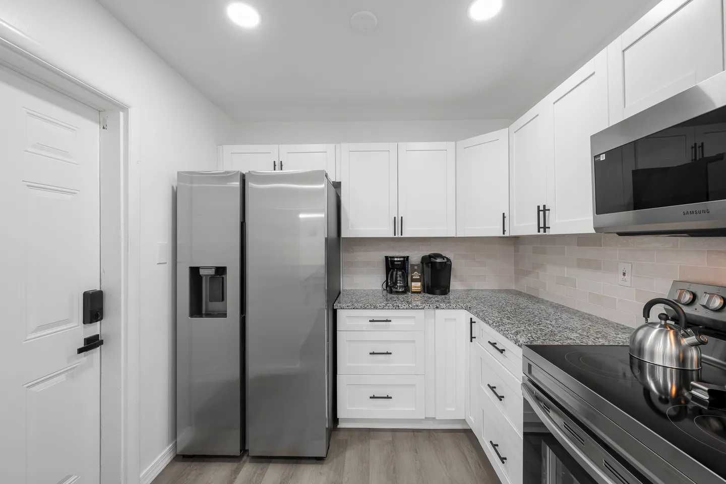 Kitchen interior featuring white shaker cabinets, speckled countertops, stainless steel refrigerator, microwave, and range.