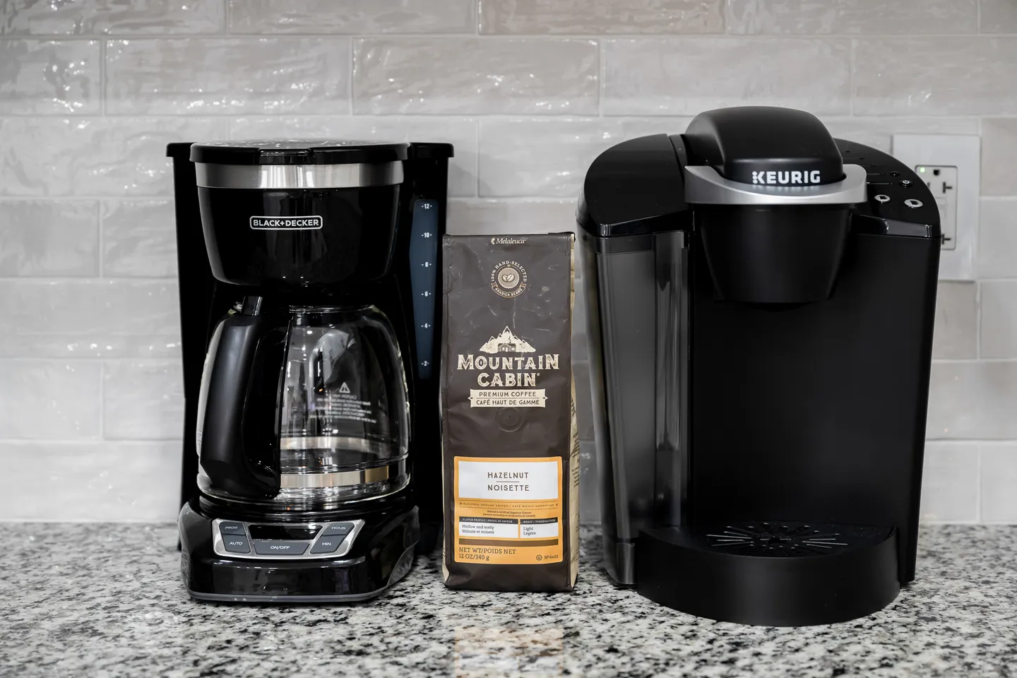 A Black and Decker drip coffee maker, a bag of hazelnut coffee, and a Keurig single-serve machine on a granite countertop.
