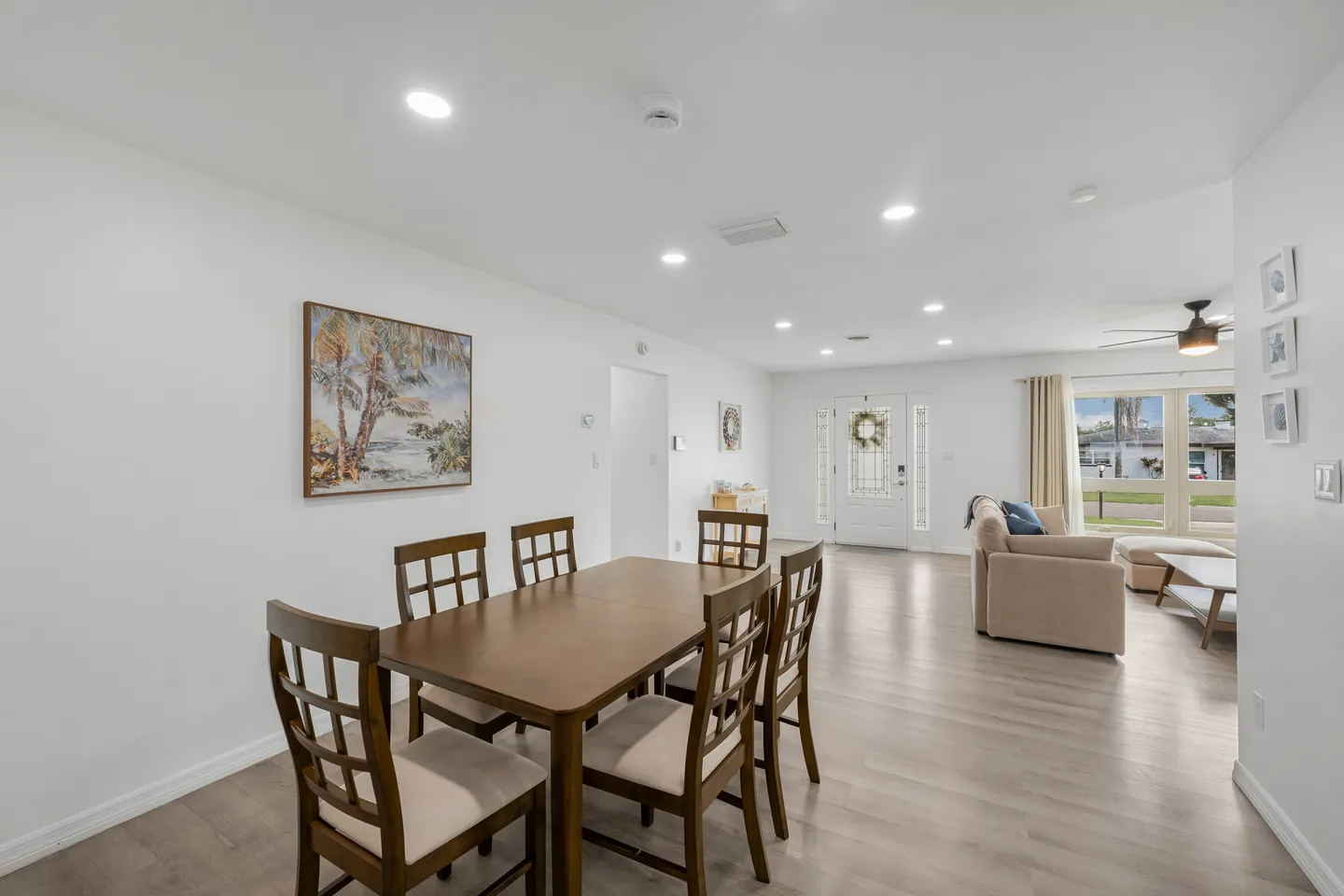 Open-concept dining and living room featuring a wooden dining table with chairs and recessed ceiling lights.