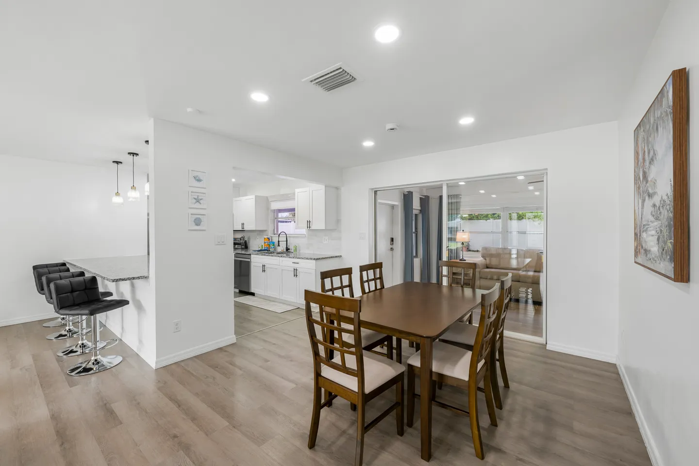 Dining area with wooden table and chairs, adjacent to a breakfast bar with black stools and an open doorway leading into the kitchen.
