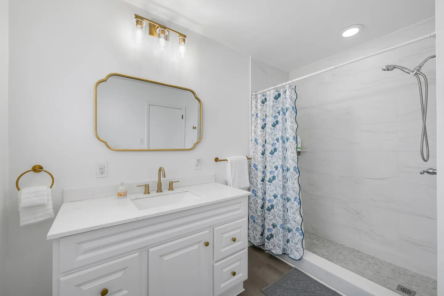 Bathroom with a white vanity, gold-framed mirror, and a walk-in shower with a floral curtain.