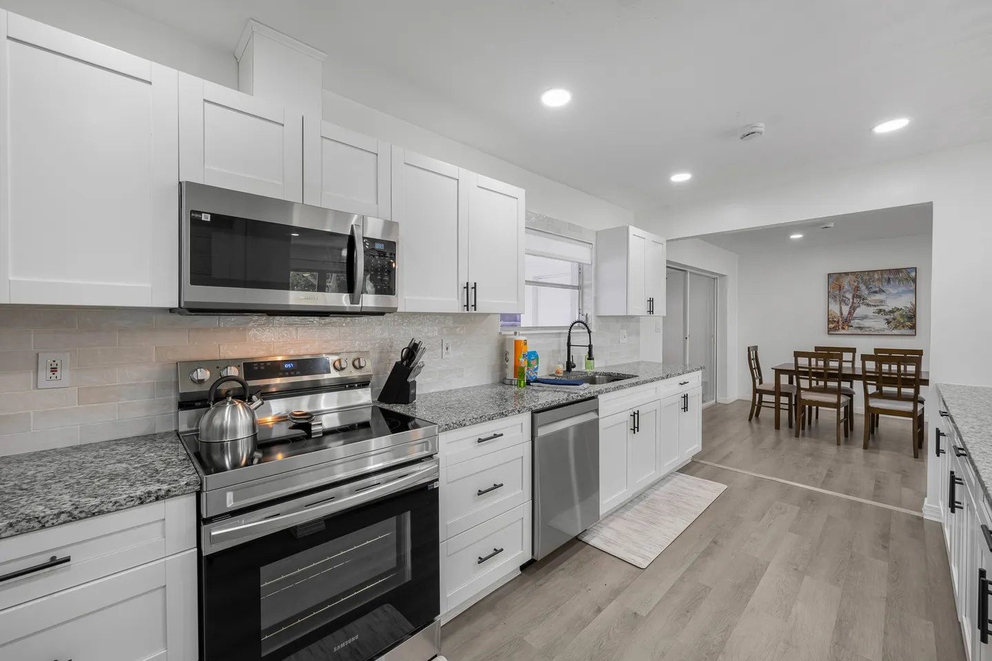 Kitchen with white shaker cabinets, speckled granite countertops, stainless steel appliances, and a view into the dining area.