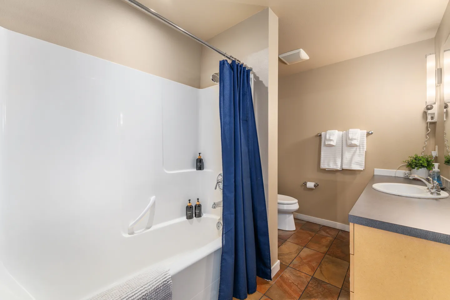 Bathroom featuring a bathtub and shower combination with a blue curtain, tiled flooring, toilet, and vanity with sink.