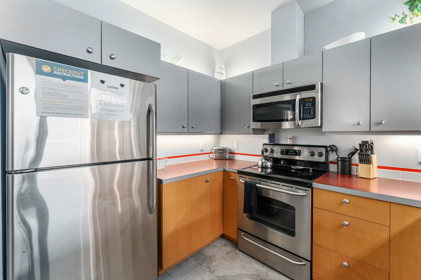 Kitchen corner featuring a stainless steel refrigerator, microwave, electric range, and two-tone cabinetry.