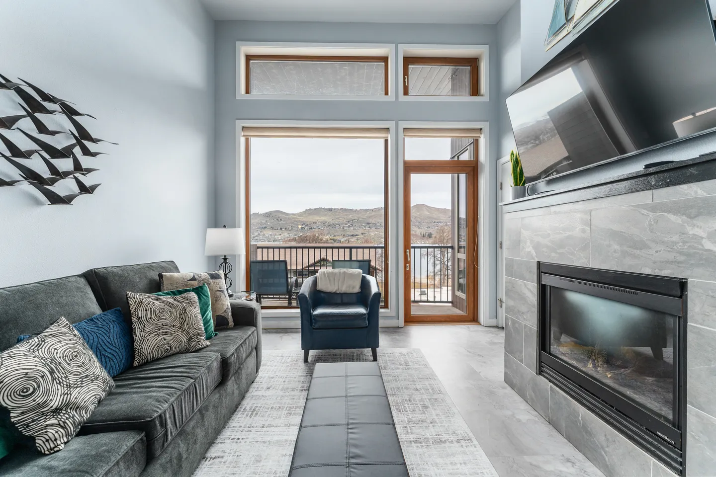 Living room with high ceilings, large windows, a tiled fireplace, and a sofa facing a TV.