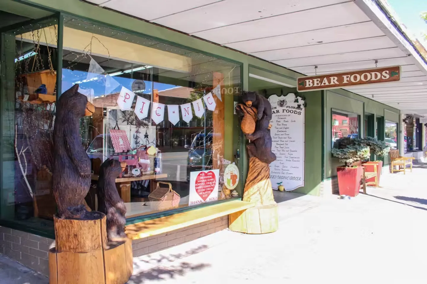 Exterior storefront of Bear Foods with large display windows, carved wooden bear statues, and a covered sidewalk.