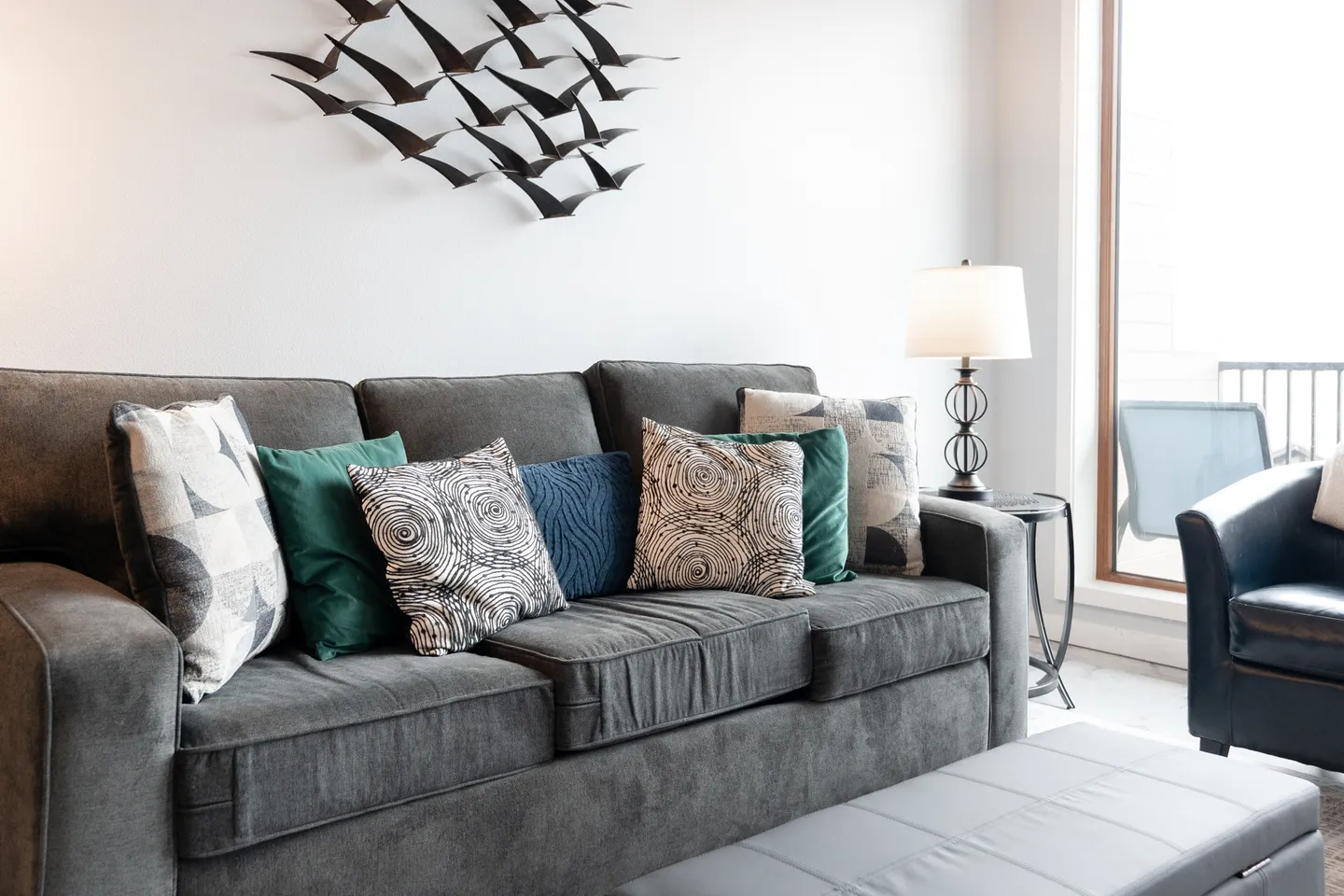 A gray upholstered sofa adorned with decorative throw pillows beneath a wall sculpture of birds in flight.