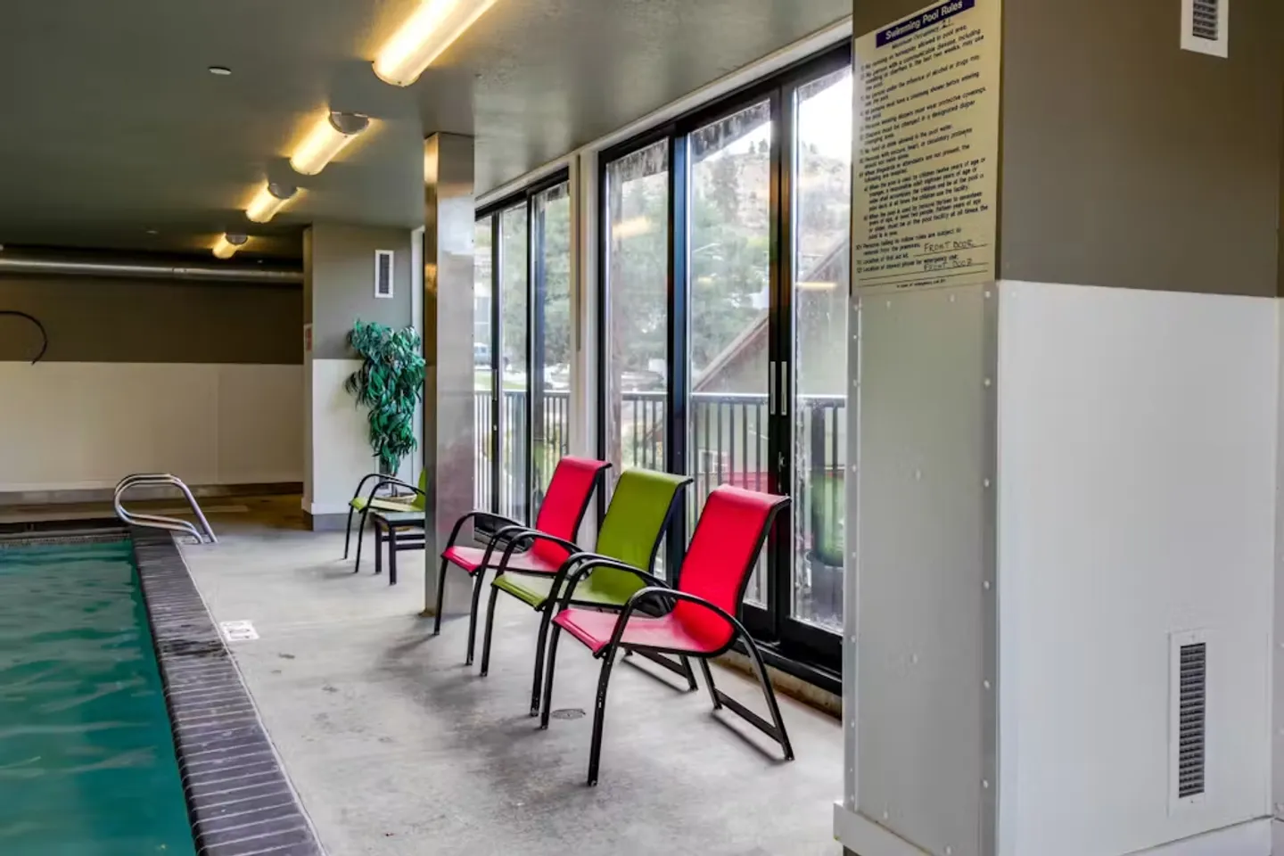 Indoor pool area with chairs lined up alongside large windows and a railing.