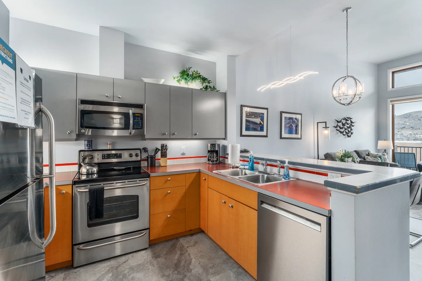 Kitchen with stainless steel appliances, two-tone gray and wood cabinetry, and a peninsula counter overlooking the living area.