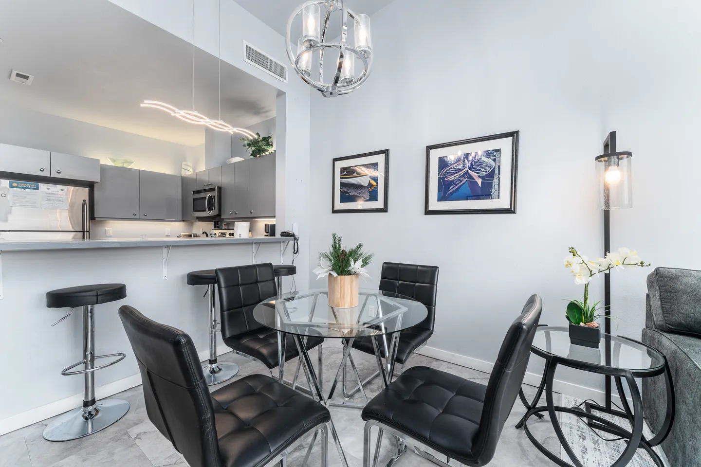 Dining area with a round glass table, black chairs, and a breakfast bar opening to the kitchen.