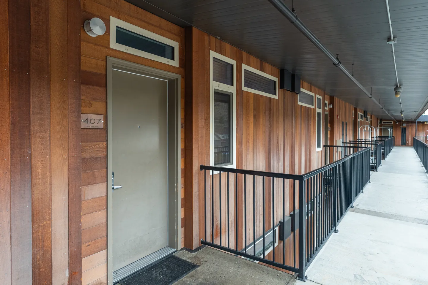Exterior open-air hallway with wood siding and entrance door labeled 407