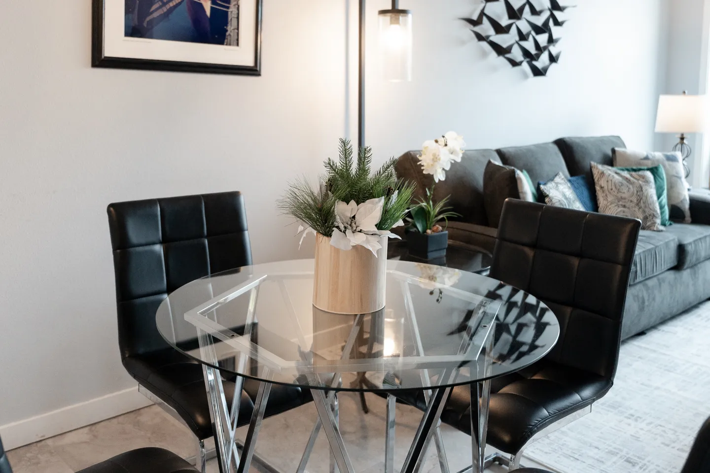 A glass-top dining table with black leather-style chairs next to a living room sofa.