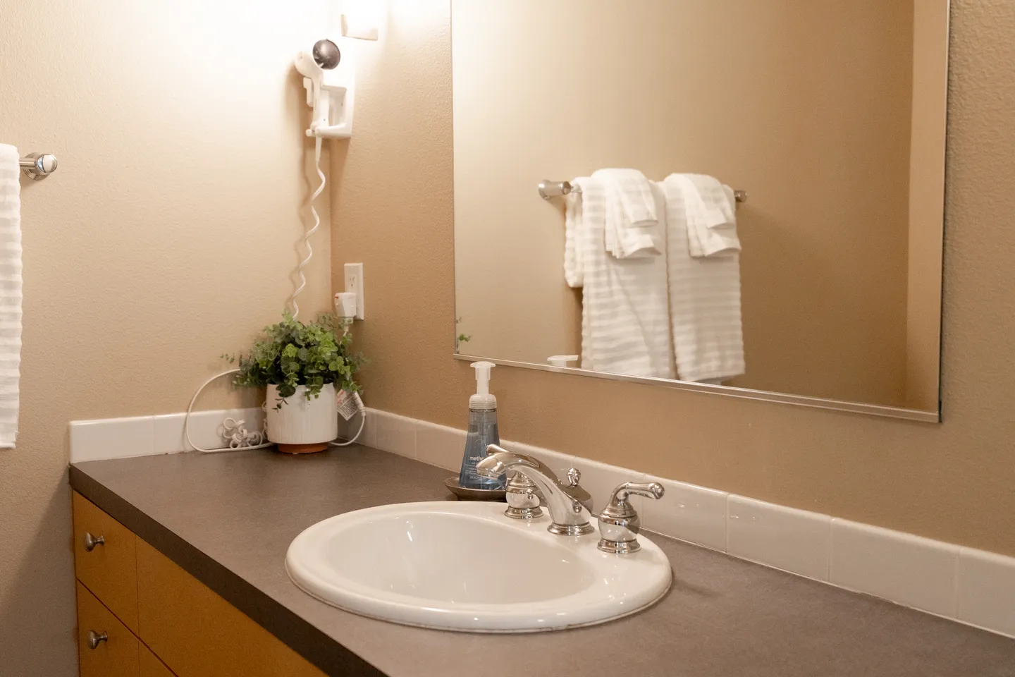 Bathroom vanity with an oval sink, chrome faucet, large mirror, and wall-mounted hair dryer.