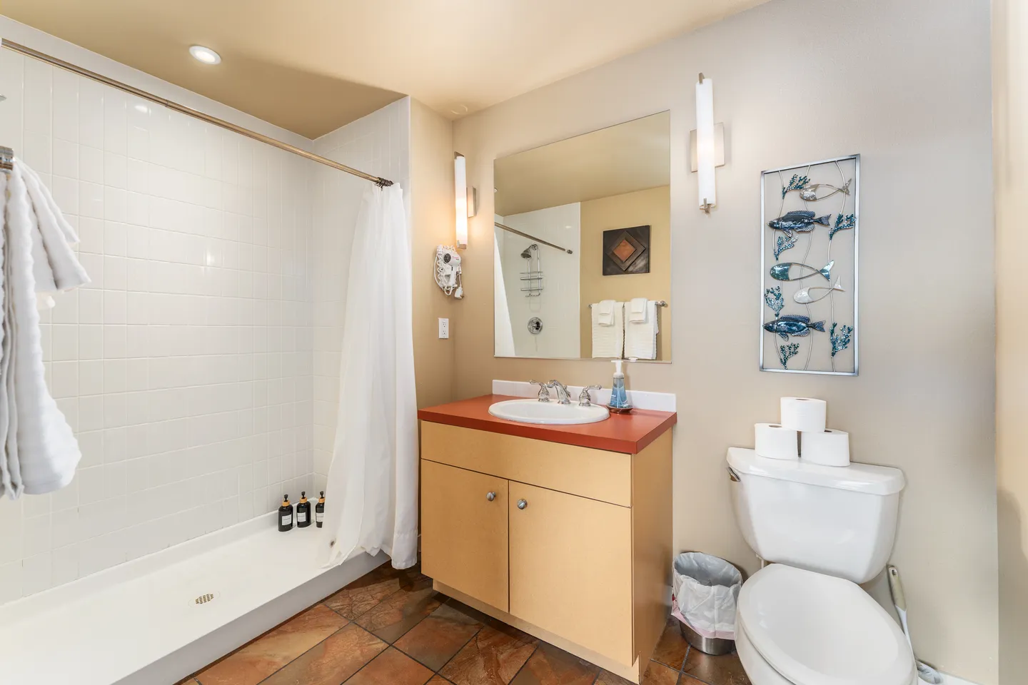 Bathroom with a walk-in tiled shower, vanity with wood-tone cabinets, a large mirror flanked by light sconces, and a toilet.