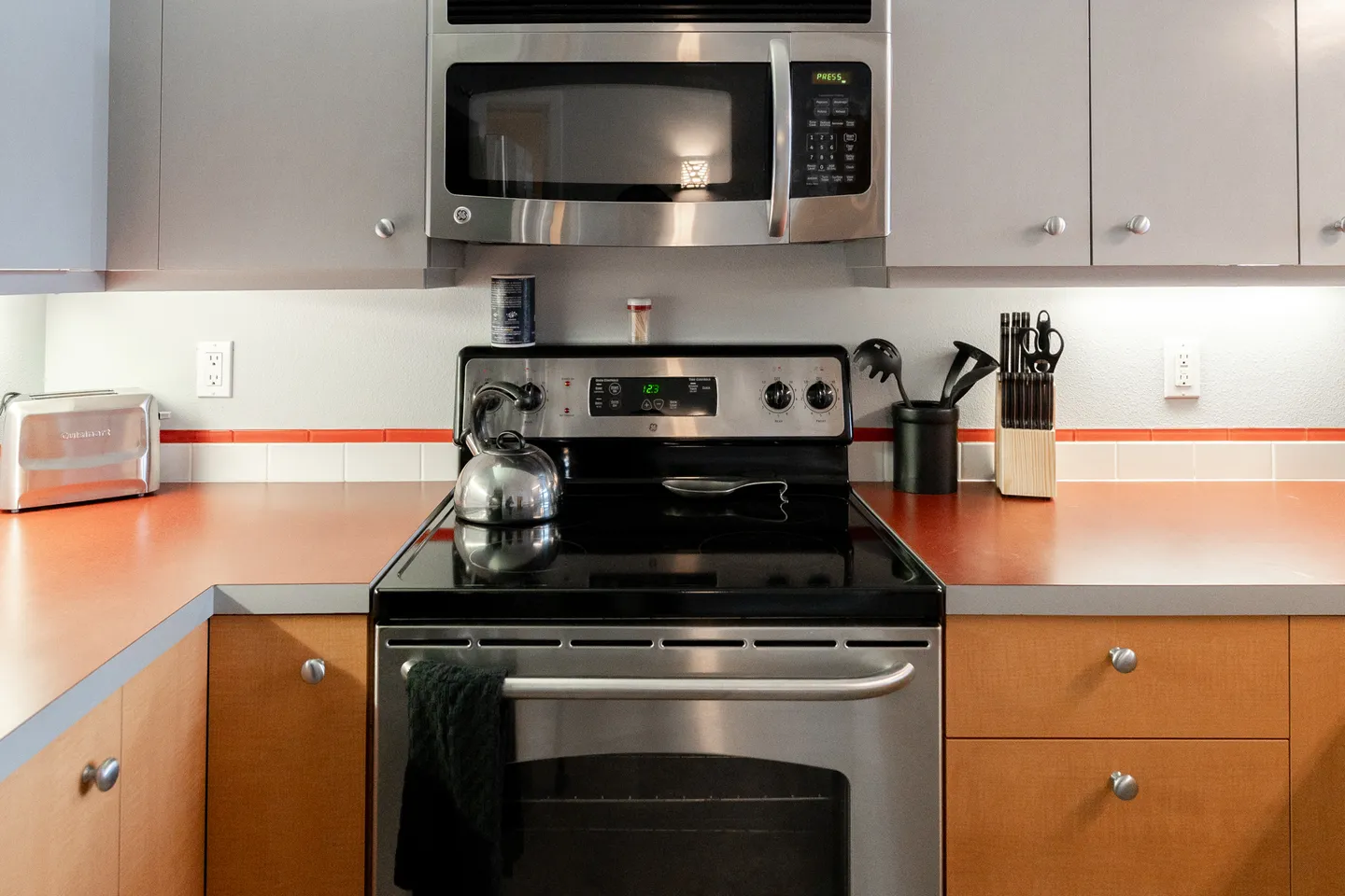Close-up of a kitchen cooking area with a stainless-steel range, over-the-range microwave, and orange-toned countertops.