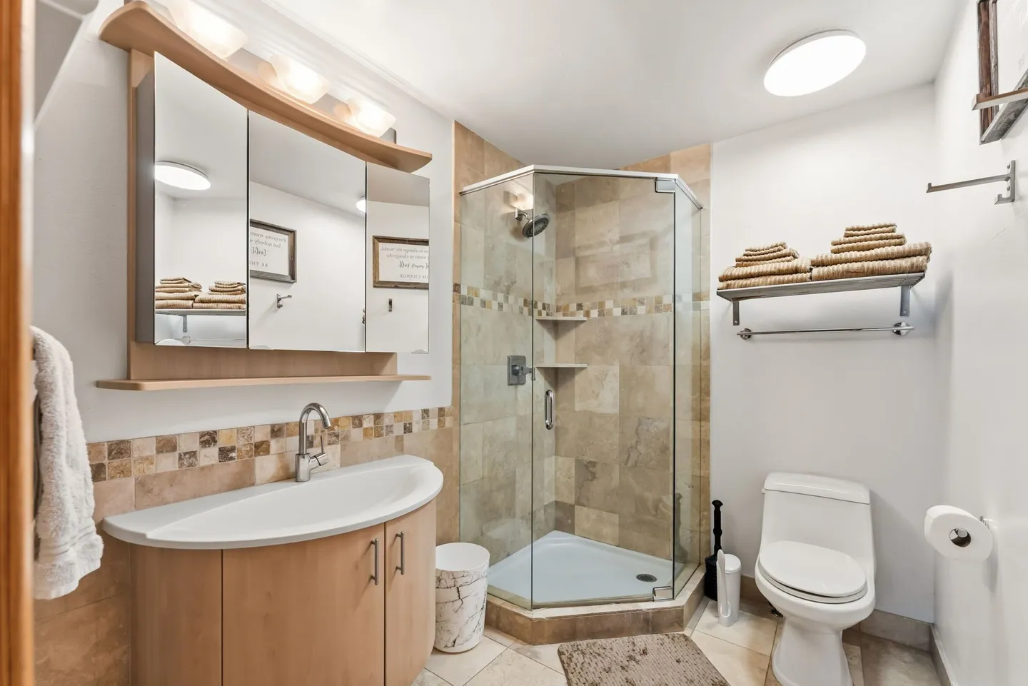 Bathroom featuring a corner glass-enclosed shower, wood vanity with curved countertop, and white toilet.