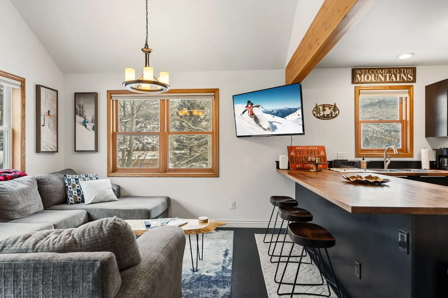 Open-concept living room and kitchen counter with sectional sofa, wall-mounted television, and bar seating.