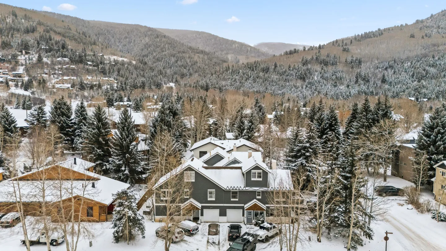 Aerial view of a multi-story building surrounded by snow and evergreen trees against a mountainous backdrop.