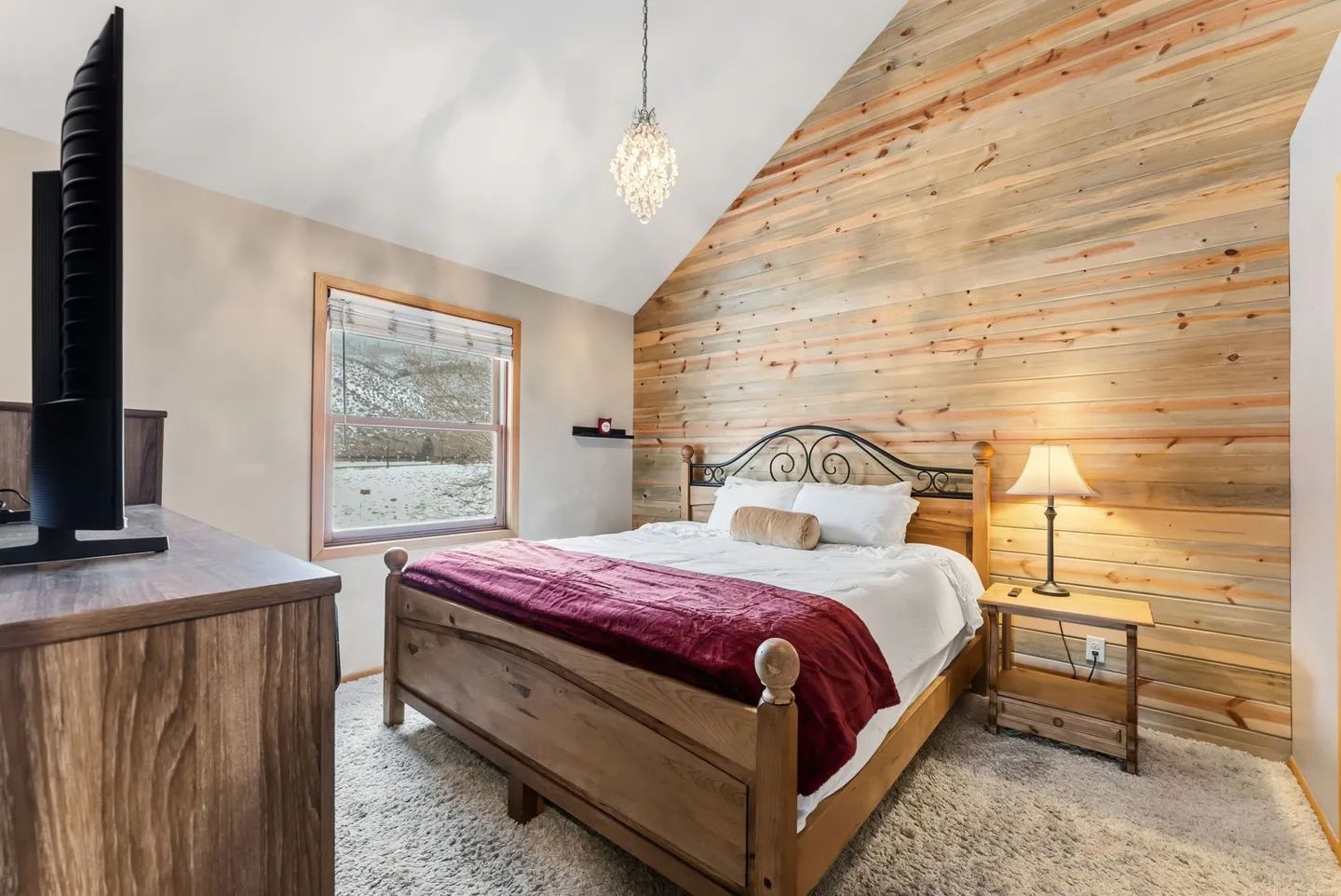 Bedroom with a wood-paneled accent wall, vaulted ceiling, and wooden bed frame.
